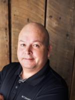 Commissioner Dustin Best, an indigenous person from the Confederated Tribes of the Colville Reservation, wearing a black shirt in front of a wooden surface.